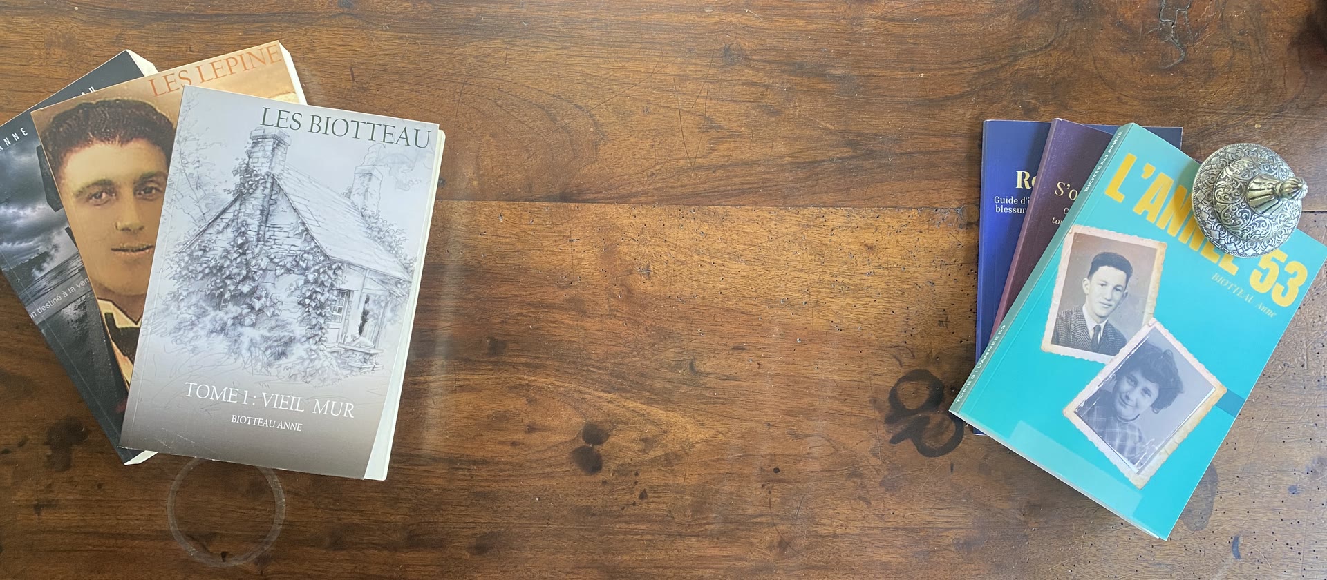 Des livres de famille écrits par Anne Biotteau, dont Les Biotteau tome 1 Vieil Mur et L'Année 53, posés sur une table en bois ancienne